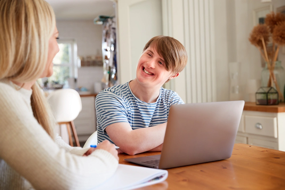 young disabled boy with laptop and smiling and looking at his carer